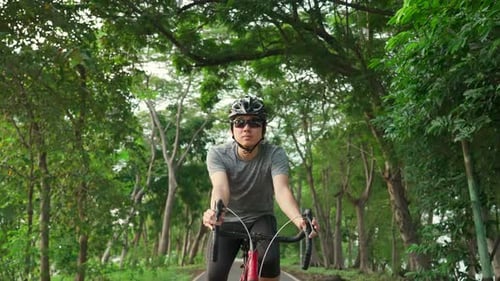 Asiatischer junger aktiver Mann, der abends für sein Wohlbefinden und seine Gesundheit im öffentlichen Park Fahrrad fährt.