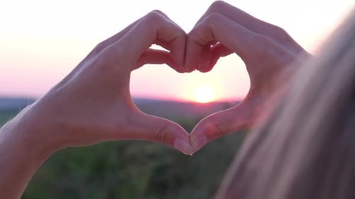 Manos femeninas en forma de corazón contra el cielo atraviesan los rayos del atardecer
