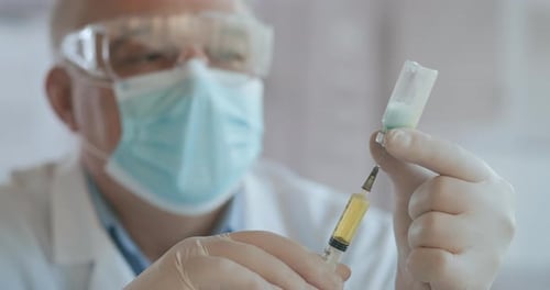 Close Up Shot of Unrecognizable Nurse or Doctor in Gloves Filling Syringe From Ampule with Covid-19