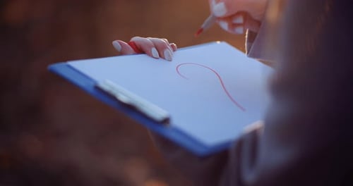 Woman Drawing Heart Symbol at Clipboard