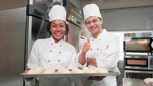 Smiling chefs holding tray of dough in kitchen