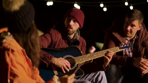 Friends Gather Around Campfire with Guitar at Night
