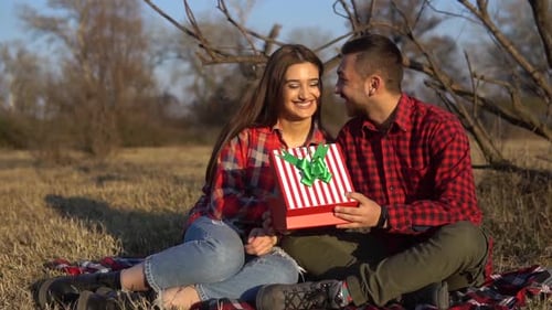 Smiling Couple Sharing a Gift in a Meadow