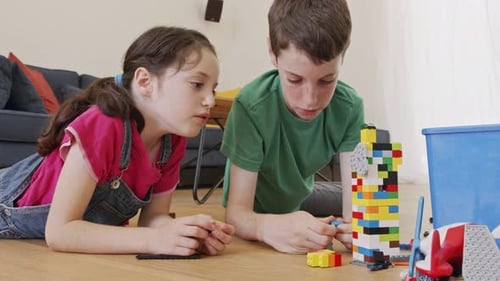 Menina e um menino brincando e construindo com tijolos de brinquedo no chão da sala