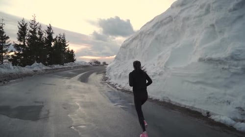 Woman Running on Snowy Road in Winter Sunset