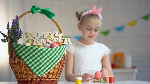 Happy Easter Sign on Basket, Cute Girl Painting Eggs Sitting at Table, Holiday