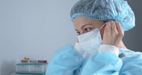 Woman doctor puts on a medical mask. Tired nurse in the clinic office.