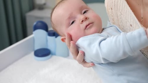 Closeup of Young Caring Mother Laying Her Little Baby Son on Dressing Table