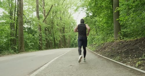 Young Male with Face Mask in Sportswear Running on the Road at Forest. Men Doing Intense Run Workout