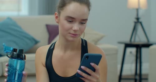 Young Woman Using Phone after Home Workout