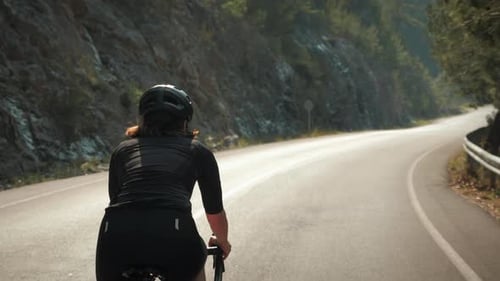 Woman Cycling Uphill Through Rural Mountain Road
