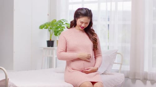 Pregnant Woman Sitting on Bed Rubbing Her Stomach