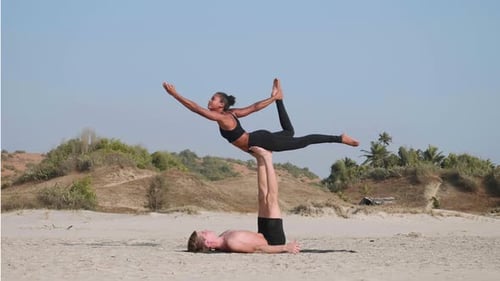 Fit Sporty Couple Practicing Acro Yoga with Partner Together on the Sandy Beach