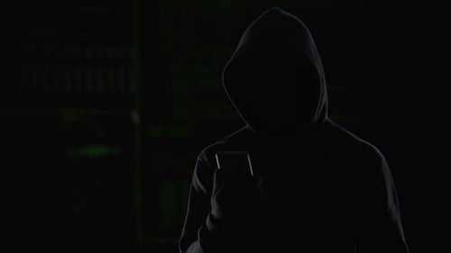 Anonymous Hooded Figure with Phone in the Dark