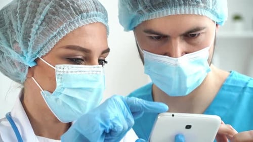 Team of Doctors in Masks Discuss Patients Diagnosis on Tablet in Clinic