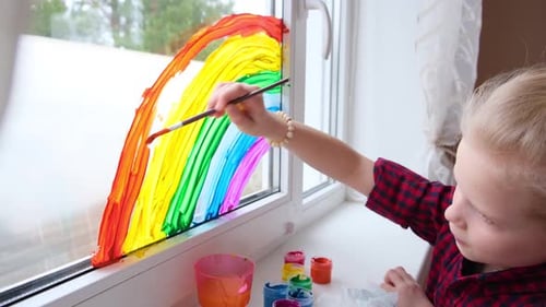 Child Painting Bright Rainbow on Window at Home