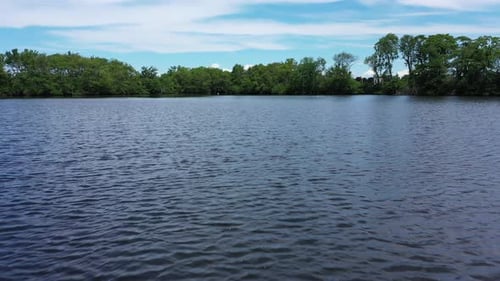 A low angle shot over a pond with gentle ripples in the water. The drone seems to hover but it does