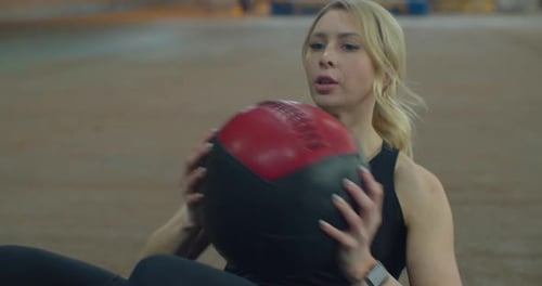 Young Caucasian Sports Woman Doing Abs Workout with Weight Ball Lying on Mat in Loft Style Gym