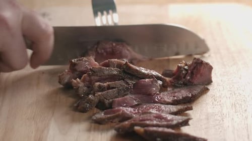 Close Slow Motion Slider Shot of a Medium Rare Steak Being Sliced with a Chef Knife and Fork.