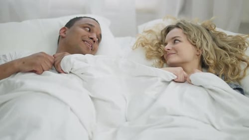 Junges glückliches tausendjähriges Paar versteckt sich unter weißer Decke kuschelt liegend im Bett