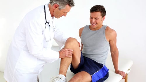 Doctor Examines Young Man's Knee in Medical Office