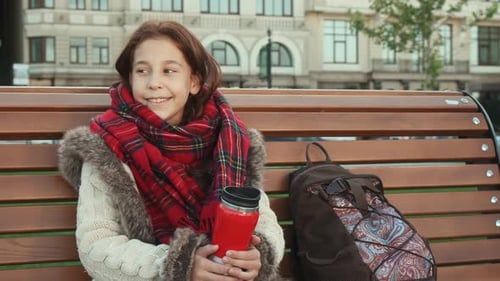 A Little Girl Is Sitting on a Bench in a Big City