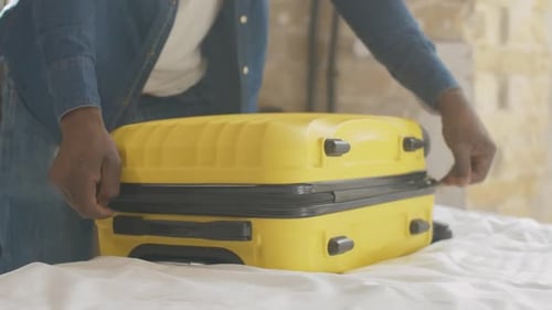 Adult Zips and Lifts Yellow Suitcase on Bed