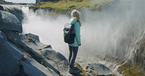 Frau steht am Klippenrand und blickt auf den mächtigen Detifoss-Wasserfall in Island