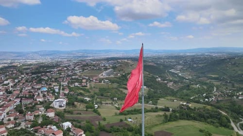 Red Flag Waving Over Green Hills, Aerial View
