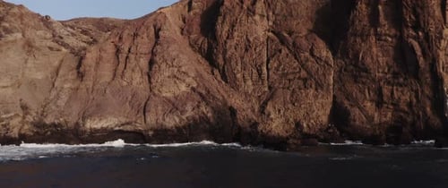 Drone shot of a rocky mountain by the wavy sea