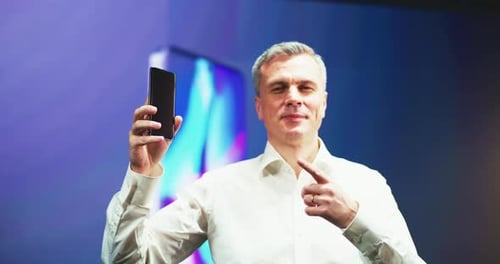 Mature Man Pointing at New Smartphone During Presentation