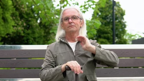 Stylish Elderly Man with Long Hair Smiling on Bench in Public City Park