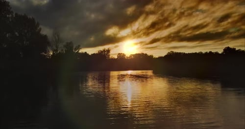 Silhouette the Sun is Reflected in the Dark Smooth Surface of the Water Trees Stand Around the River