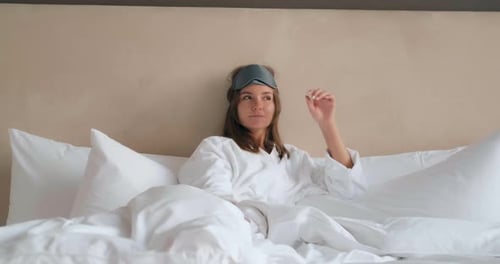 Une femme avec masque de sommeil et pyjama est allongée sur un lit confortable