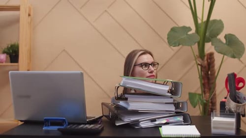 Büroangestellte sitzt am Schreibtisch vor vielen Ordnern mit Dokumenten, die menschliche Hände ablegen