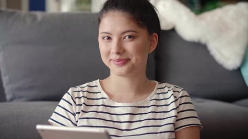 Woman Smiles Holding Tablet in Front of Couch