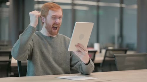 Young Man Celebrating Success on Tablet in Office