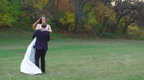 Young Groom Spins Attractive Bride Around in the Center of an Autumn Park. Happy Loving Newlyweds in