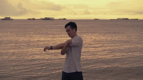 A handsome Asian sportsman stretching exercises before running exercise outside on the beach.