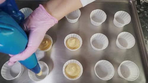 Person Filling Cupcake Liners with Dough on Tray