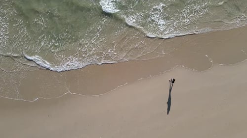 Luftaufnahme einer Person, die am Strand spaziert und Wellen einkrachen