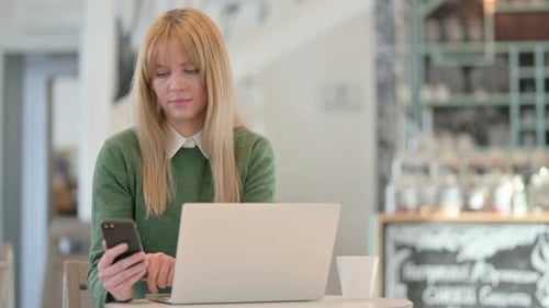 Young Woman Working on Smartphone and Laptop in Cafe in Cafe