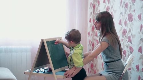 Mom Helps Son Draw a Rays of Sun on a Blackboard