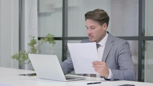 Man Working With Laptop and Documents in Office