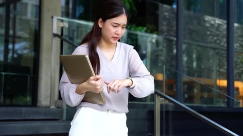 Asian Female Businesswoman Looking at Wristwatch and Checking Time at Modern Office Building Outside