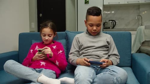 Two Children Using Phones on Couch at Home