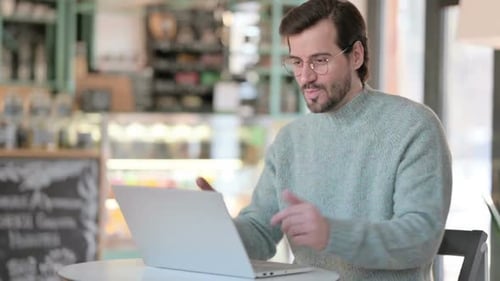 Young Man Talking on Video Call on Laptop in Cafe