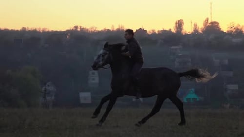 Kerl bei Sonnenuntergang springt auf einen Hengst
