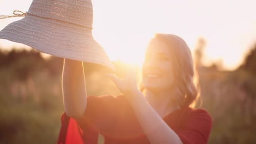 Smiling Woman Holding a Straw Hat in Field