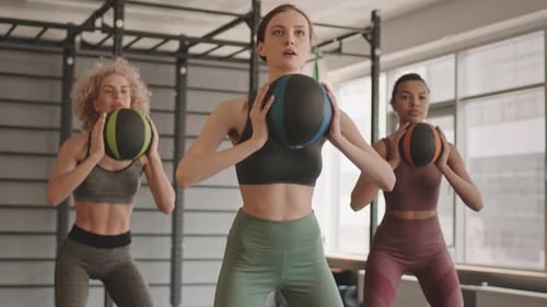 Women Squatting with Medicine Balls in Gym